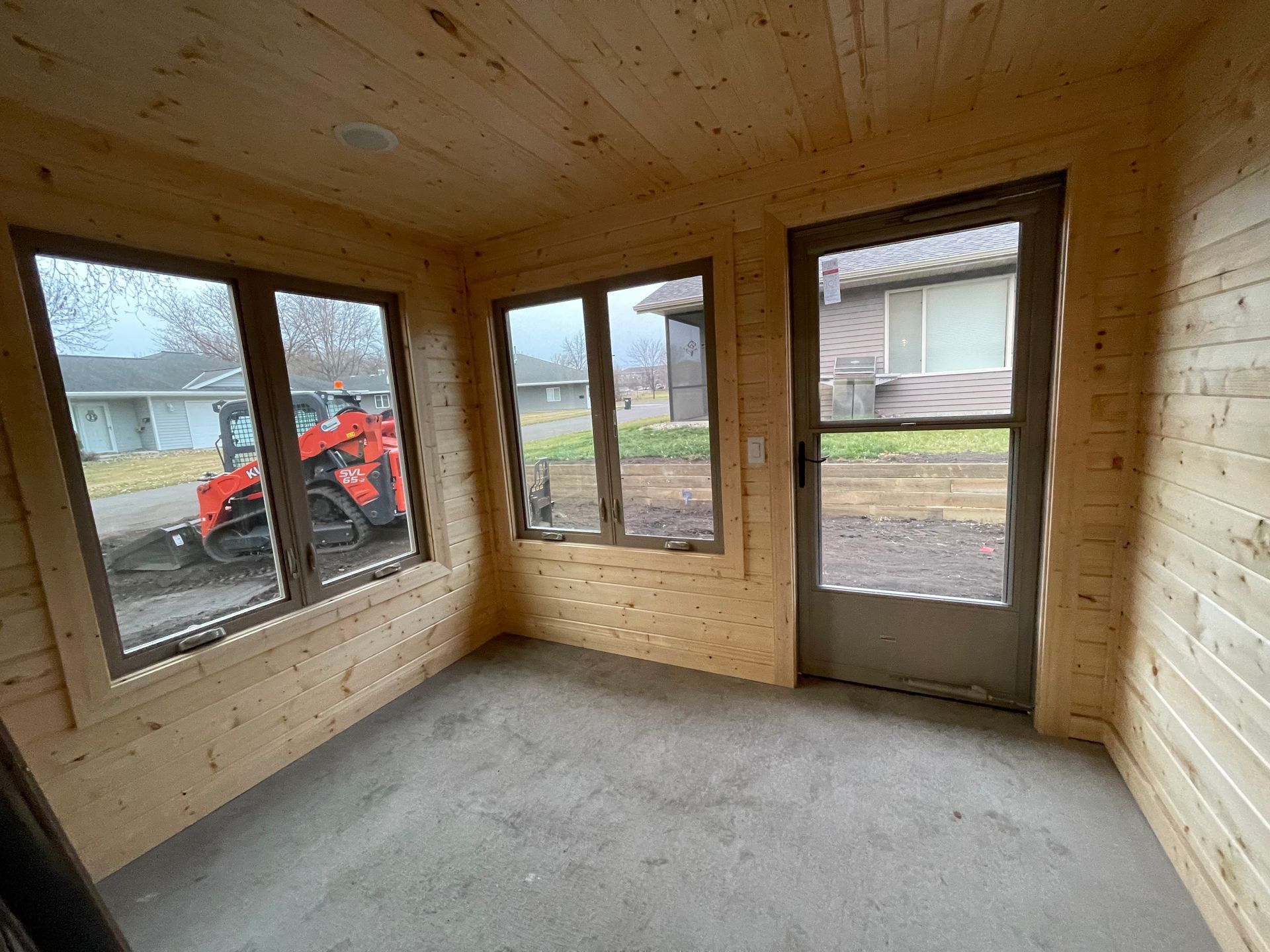 Interior view of a small room under construction, with wood paneling and windows looking out onto a street.