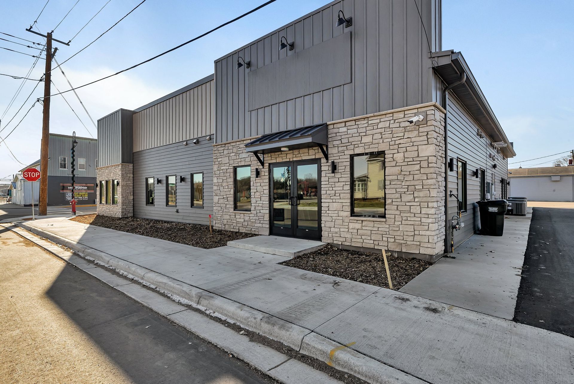 Gray and stone building with dark trim, double doors, and sidewalk.
