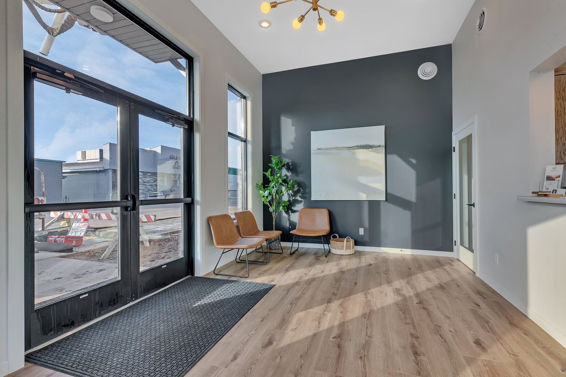 Modern office waiting area with large windows, three chairs, and abstract art on a dark gray wall.