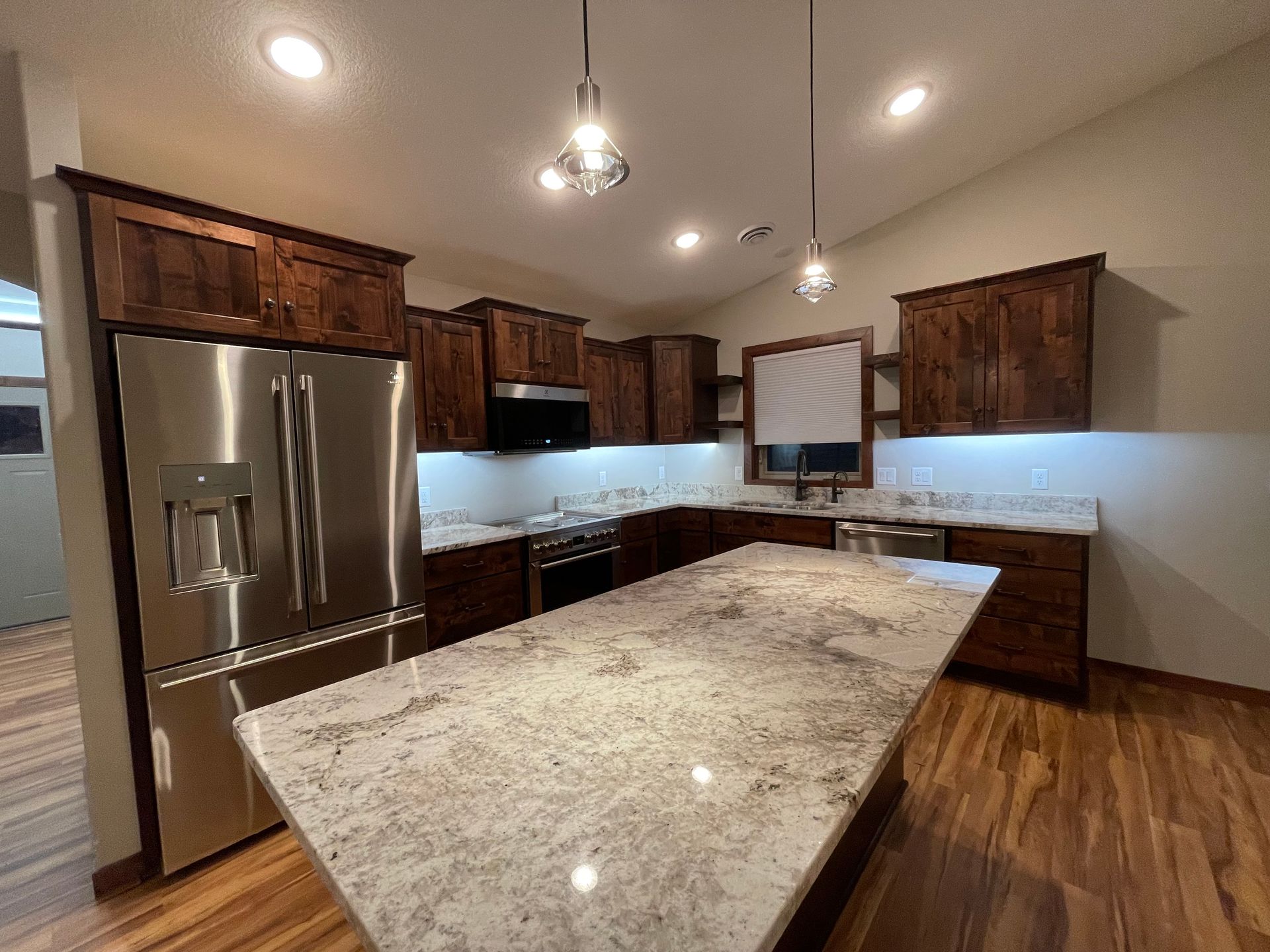 Kitchen with granite countertops, wooden cabinets, stainless steel refrigerator and island, hardwood floor.