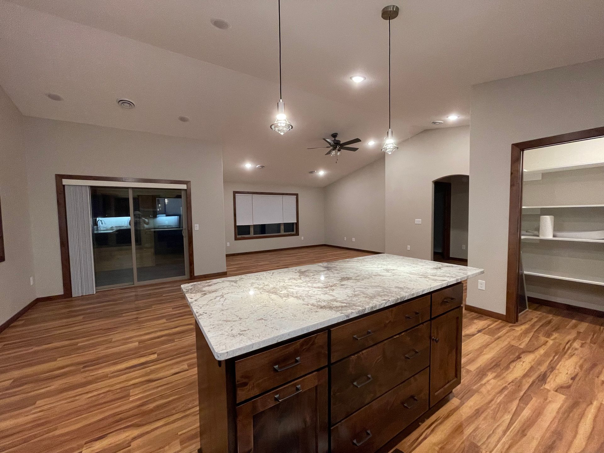 Kitchen with a dark wood island, granite countertop, and pendant lights. Hardwood floors and a pantry are also visible.