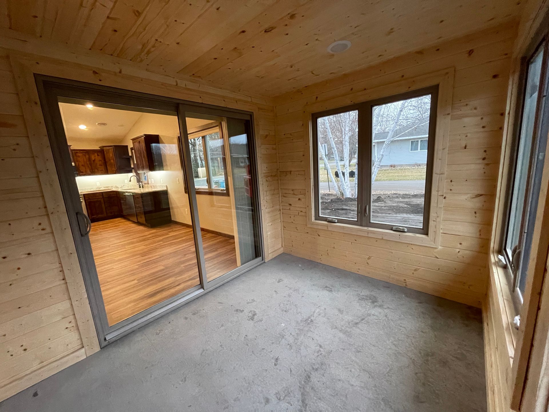 Interior of a room with wood paneling and sliding glass door leading to a kitchen.