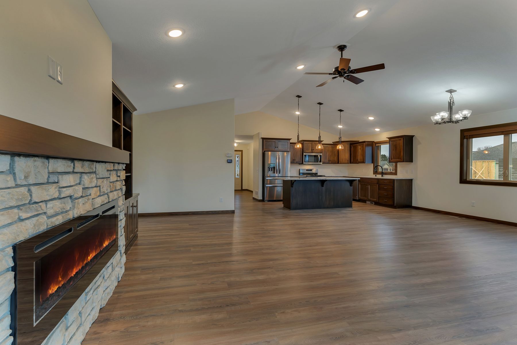 Open-concept living space with fireplace, kitchen island, wood floors, and warm-toned cabinetry.