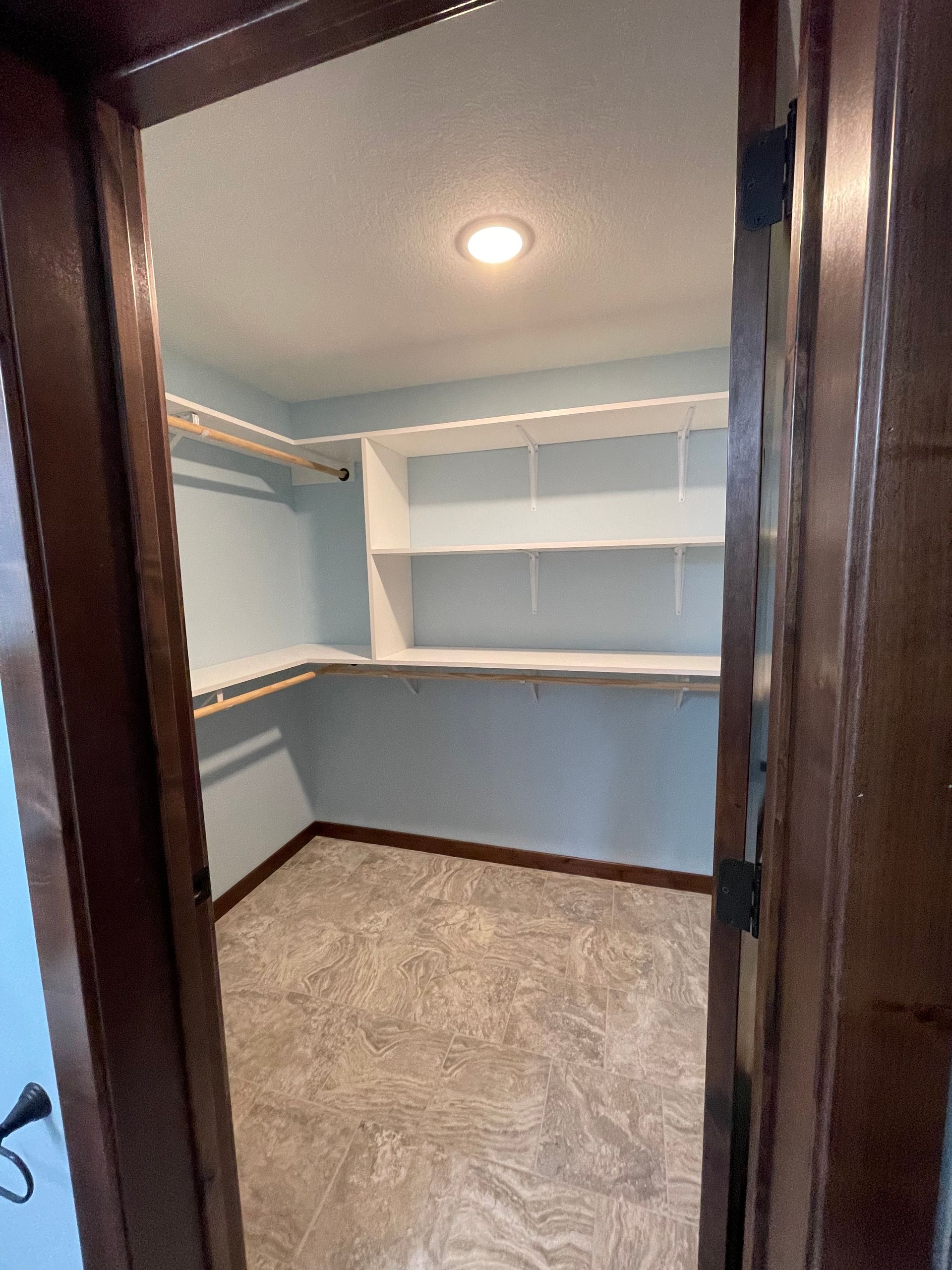 Walk-in closet with shelves and hanging rods. Blue walls, white shelving, and brown trim.