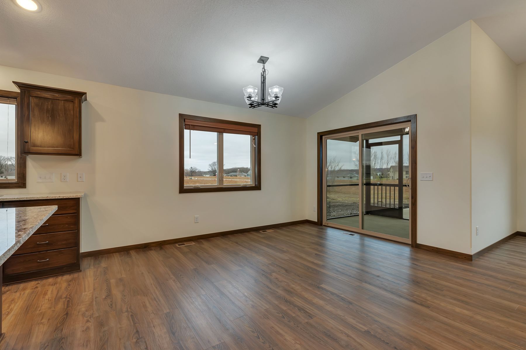 Dining room with wooden floor, cabinets, window, sliding glass door leading to a porch.
