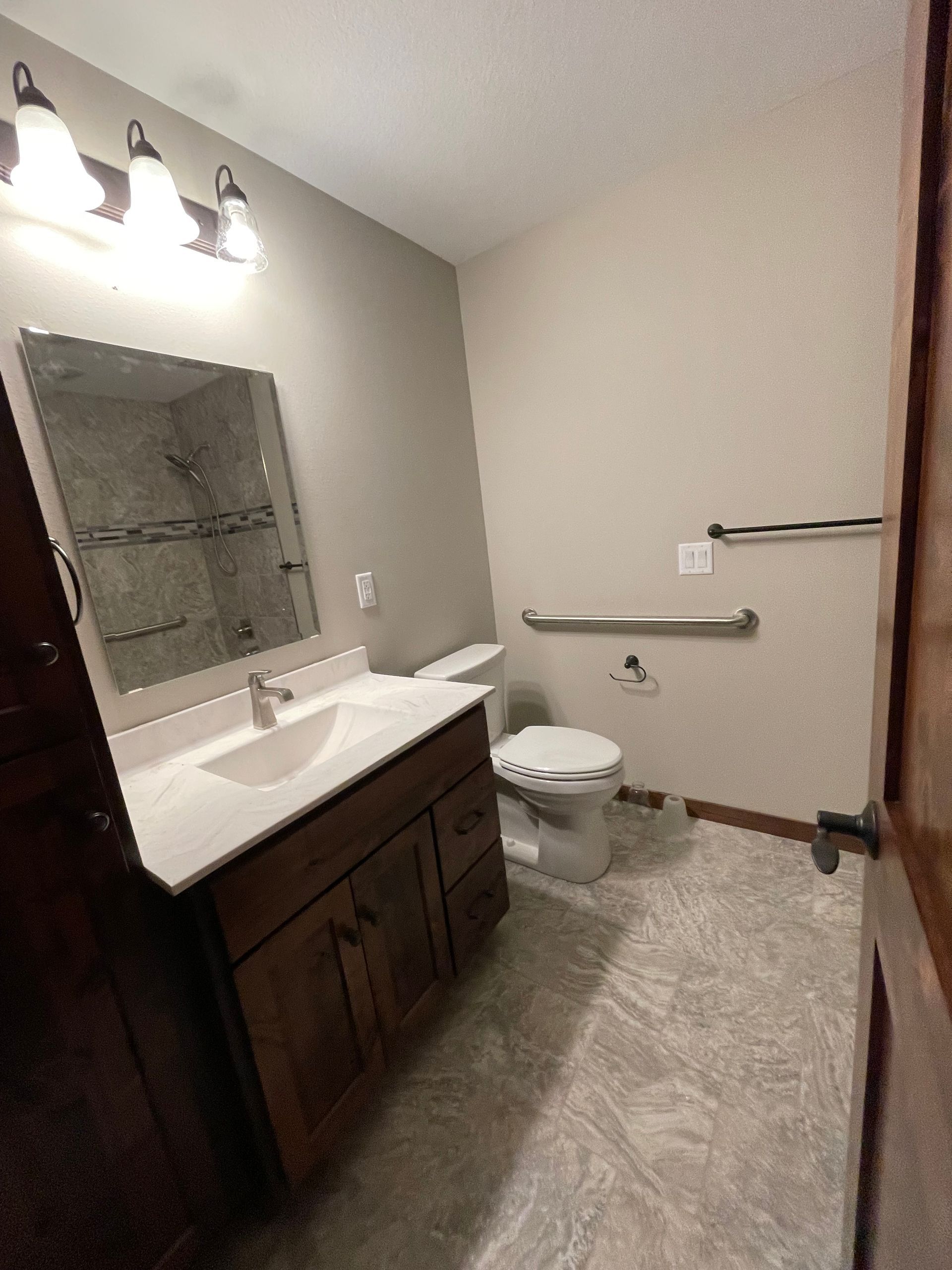 Bathroom with vanity, toilet, and grab bar; neutral color scheme.
