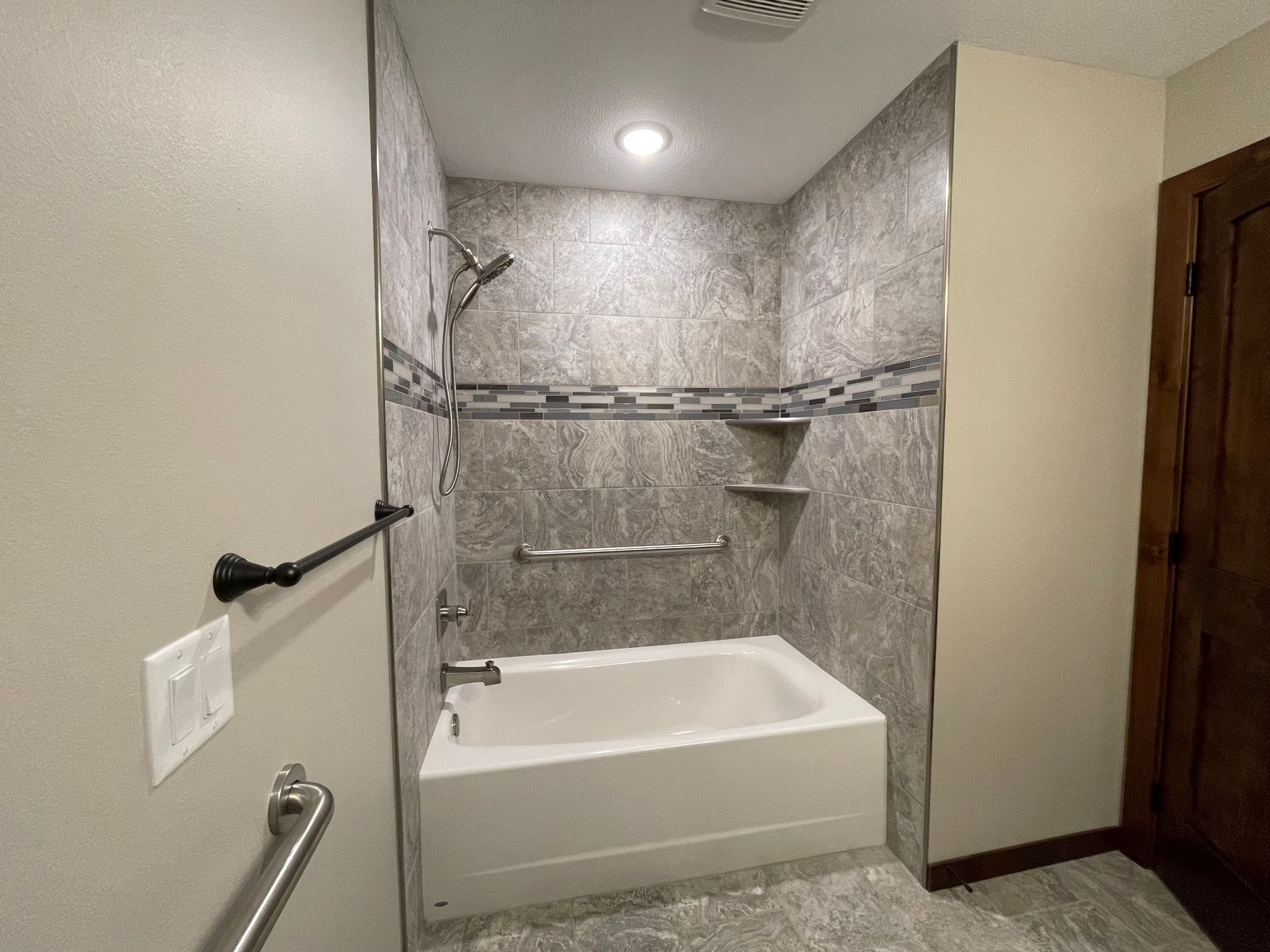 Accessible bathroom with tub, grab bars, and tiled shower walls.