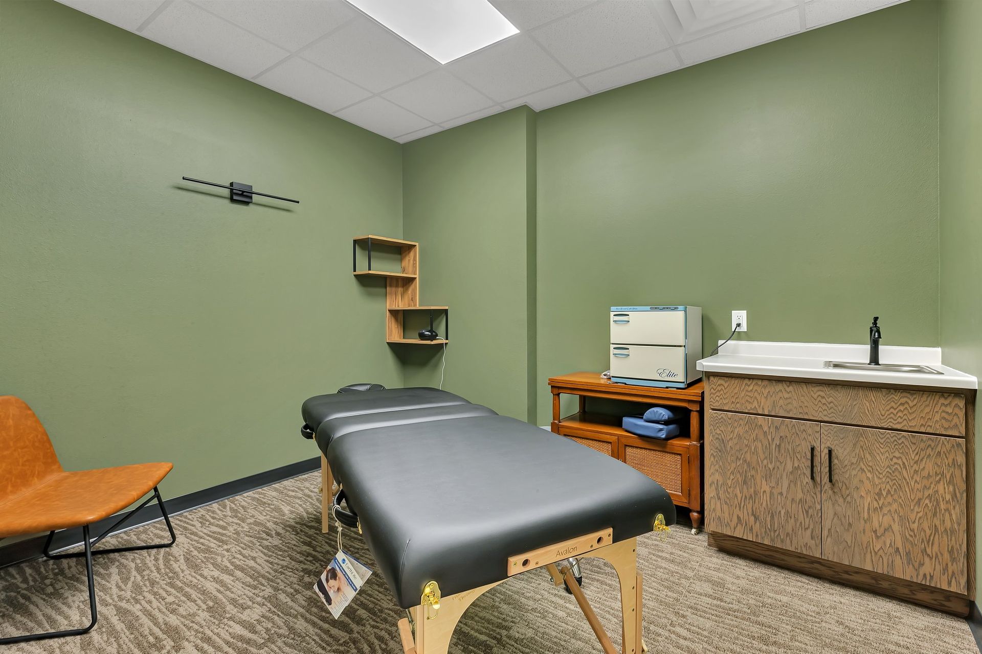 Massage therapy room with olive green walls, massage table, sink, and storage cabinet.