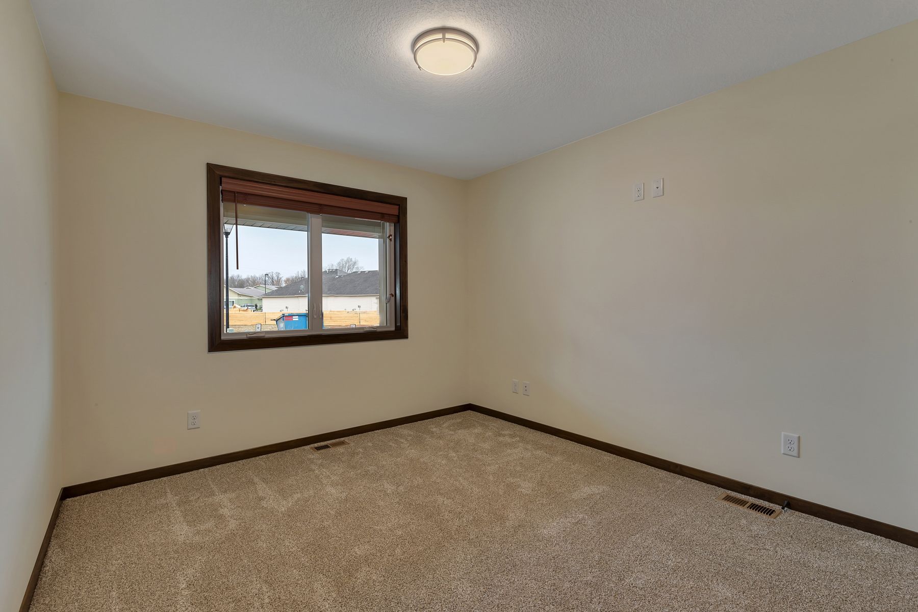 Empty bedroom with beige carpet, window, and off-white walls.