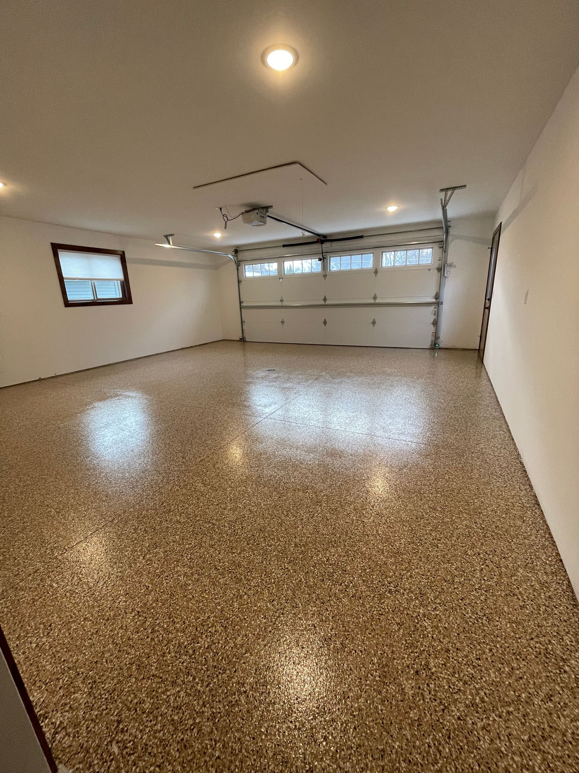 Empty garage with speckled epoxy floor, closed garage door, and a small window.