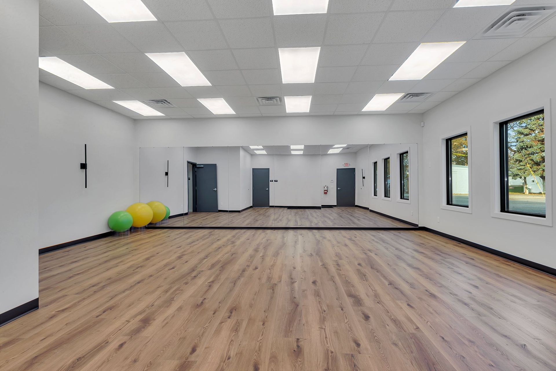 Empty studio with wood floor, large mirrors, white walls, and bright overhead lights.