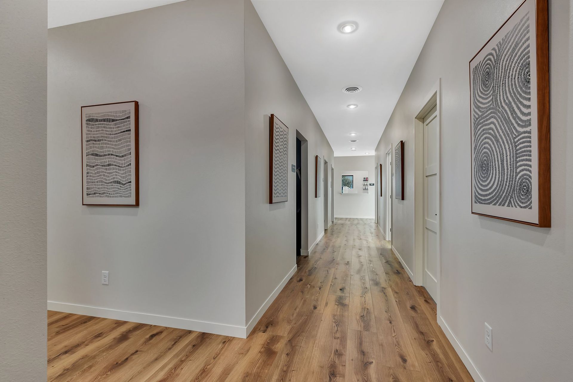 Hallway with wood floors, light gray walls, white trim, recessed lights, and framed artwork.