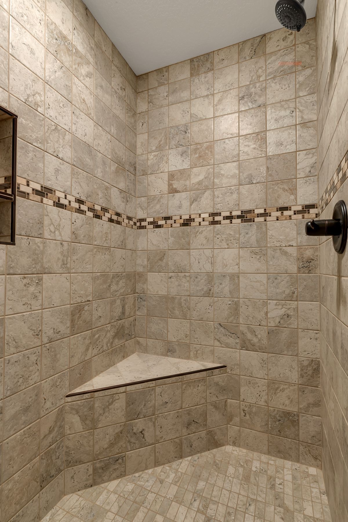 Tiled shower with corner seat and decorative tile border. Brown, beige, and mosaic tiles are visible.