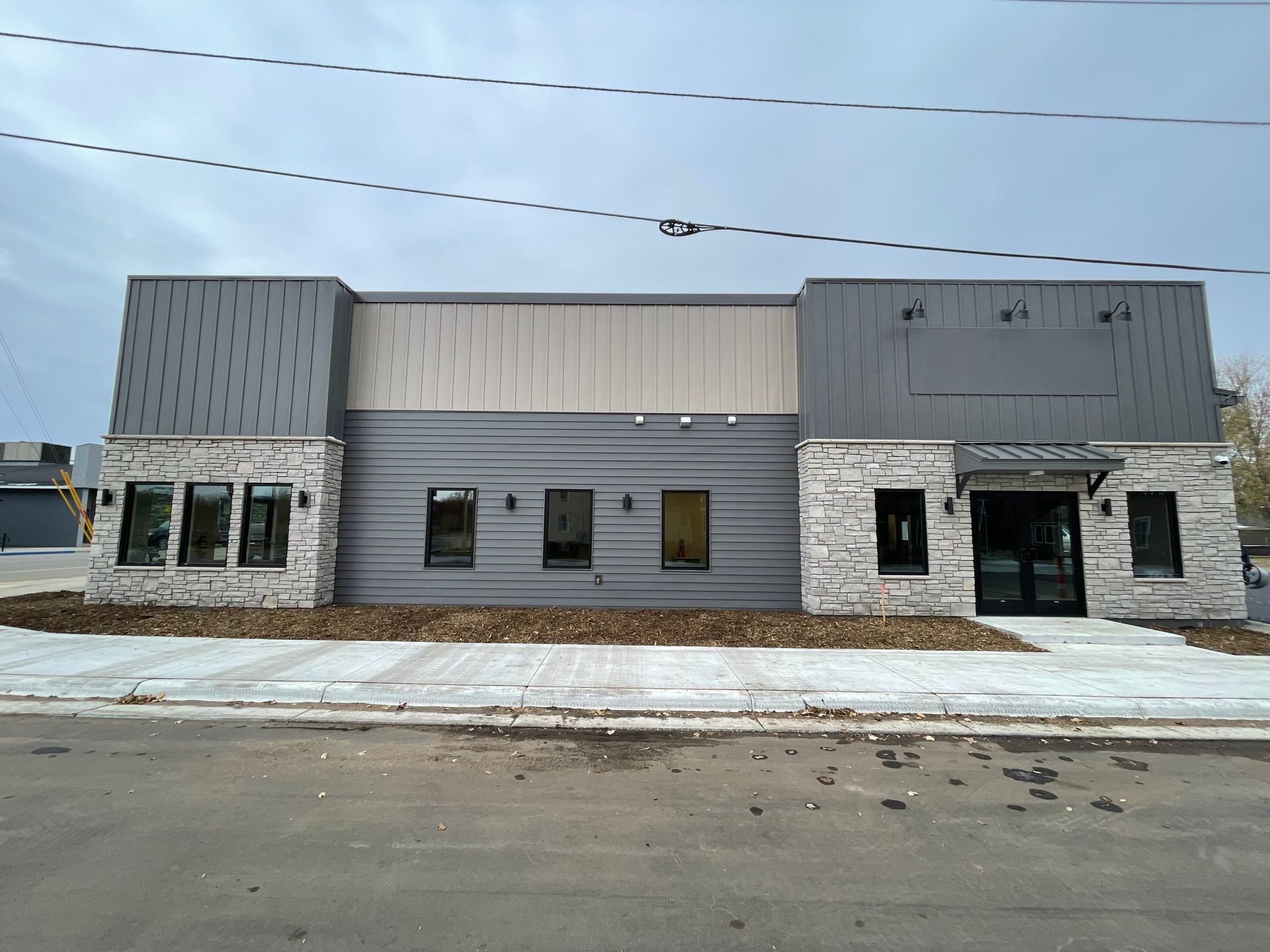 Exterior of a modern building with gray and stone facade; windows and entrance visible.