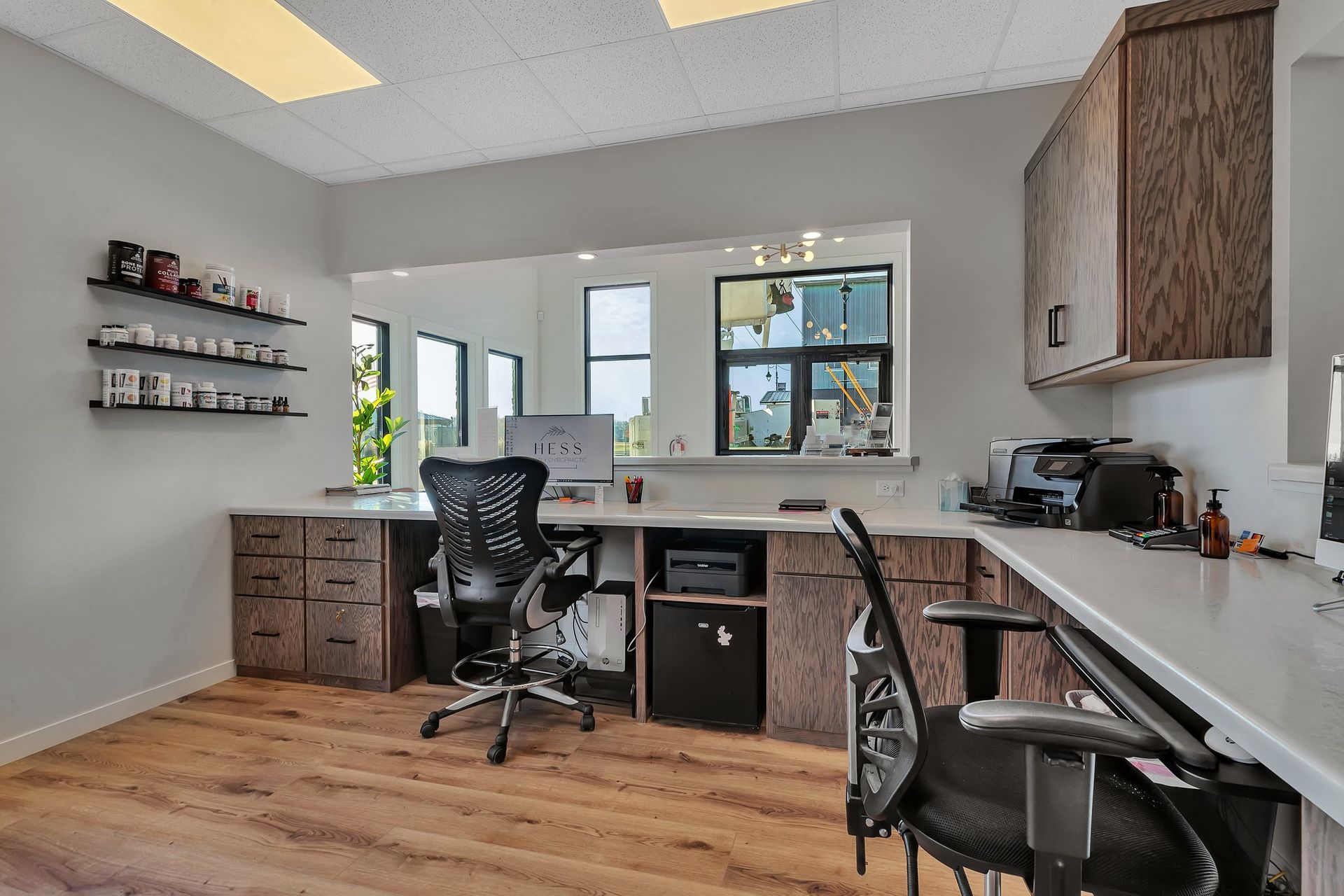 Reception area with desks, cabinets, and a large mirror. Two chairs face the desk with a printer and computer.