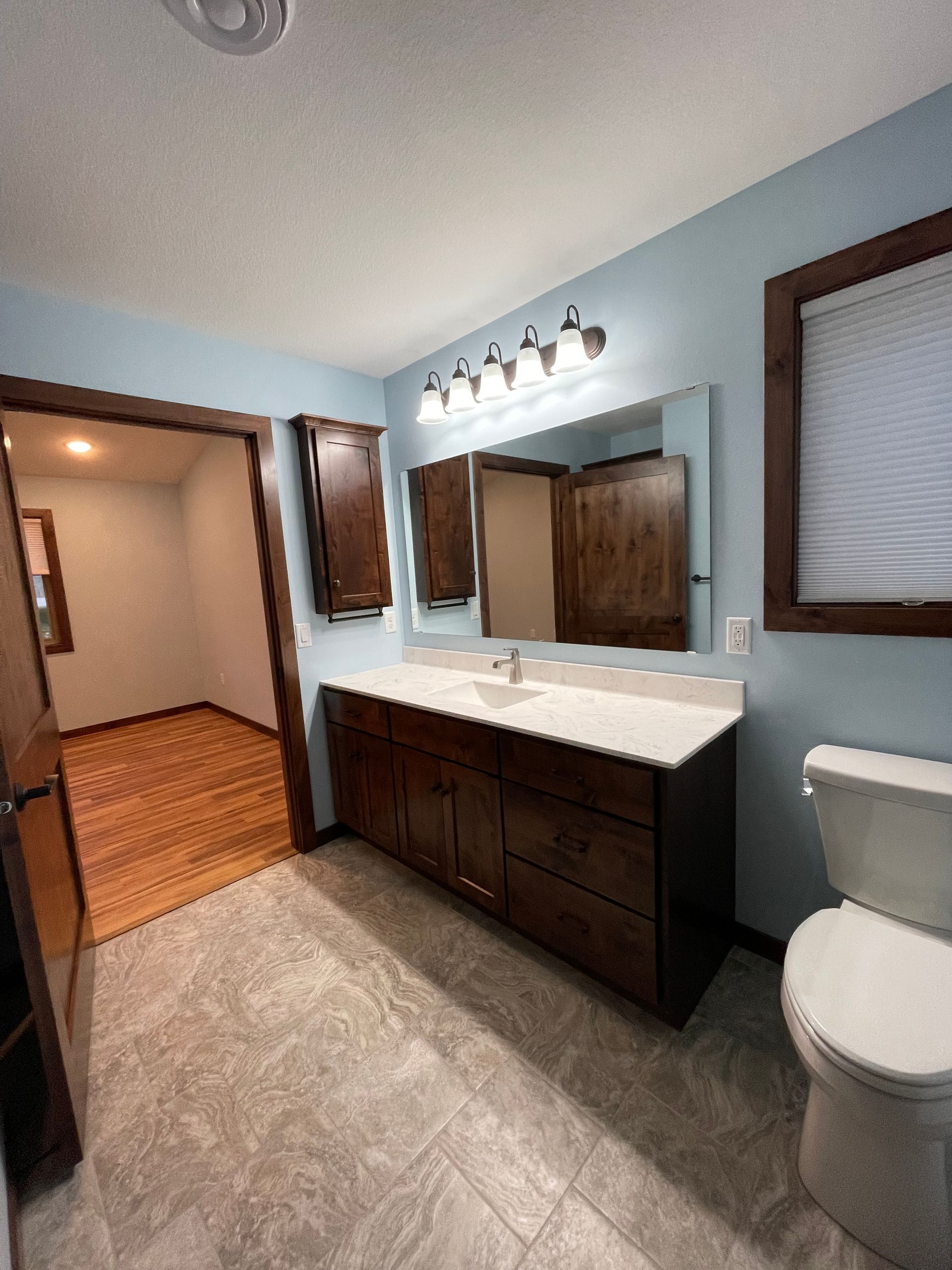 Bathroom with vanity, toilet, and doorway to a room with hardwood floors. Blue walls, brown cabinets.