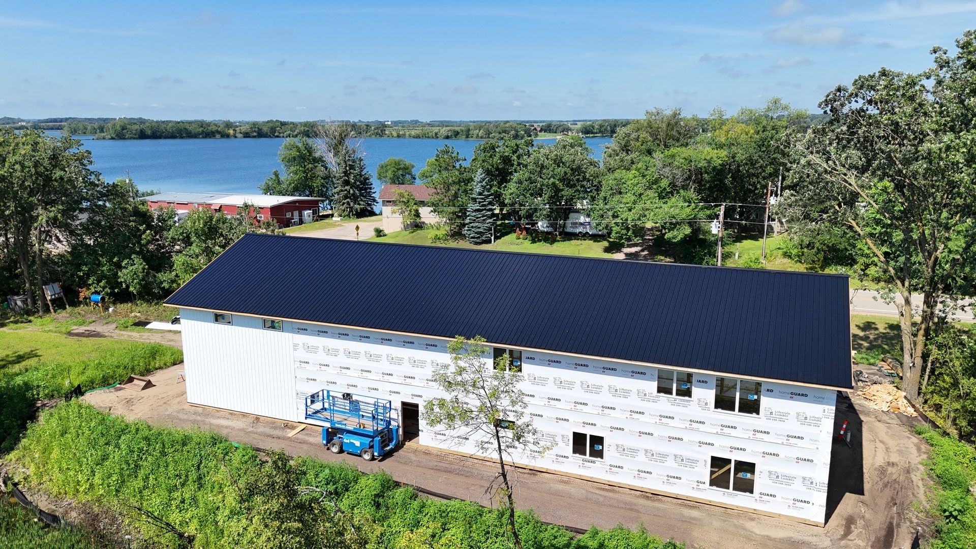 Aerial view of a white building with a dark roof near water and trees on a sunny day