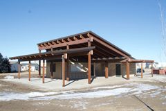 Open-sided wooden pavilion under construction on a snowy lot, with exposed beams and columns.
