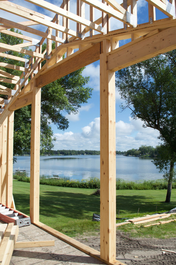 Wooden house frame under construction beside a lake with trees and clear sky