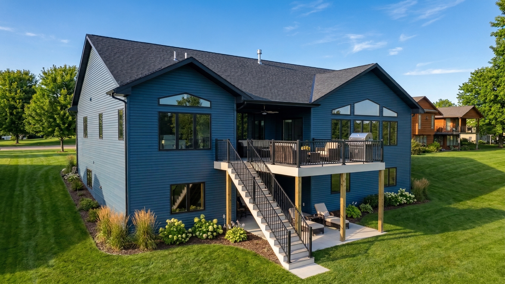 Blue-gray house with deck, stairs, and lake view on a sunny green lawn