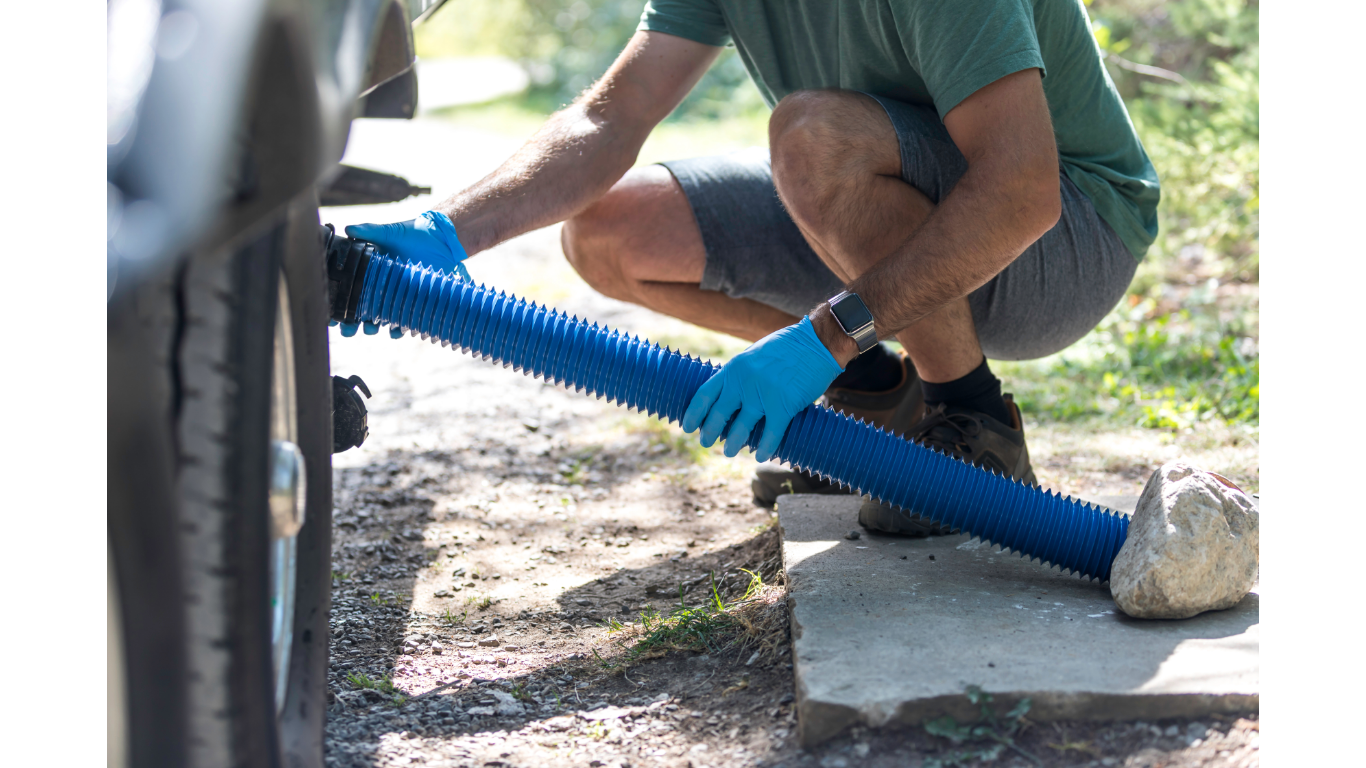 Person in blue gloves positioning a blue RV sewer hose, outdoor setting.