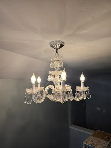 Crystal chandelier hanging from a white ceiling with four lit candle-shaped bulbs.