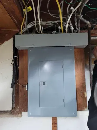 Electrical panel mounted on wood, with wires overhead. Gray panel door closed.
