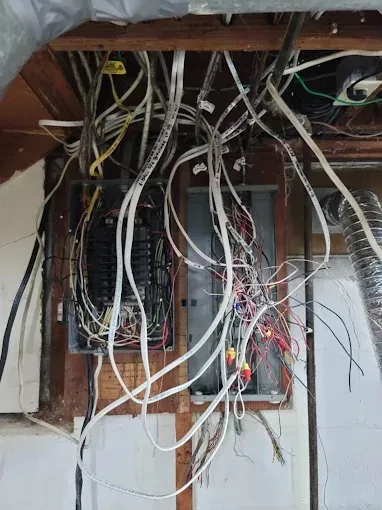 Electrical panel with tangled wires in exposed wall.