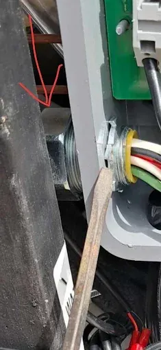 A person using a crowbar on electrical wiring, inside an appliance or machine.