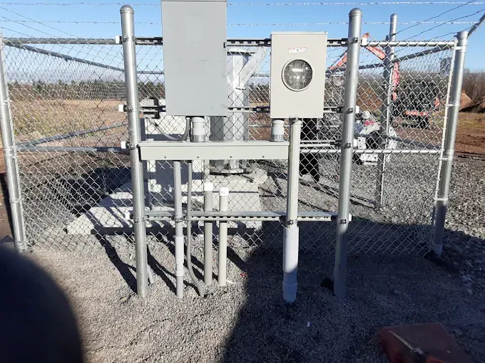 Electrical equipment enclosure within a chain-link fence, outdoors on gravel.