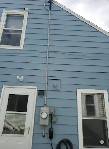 Blue house exterior with electrical meter, conduit, windows, door, and EV charger.