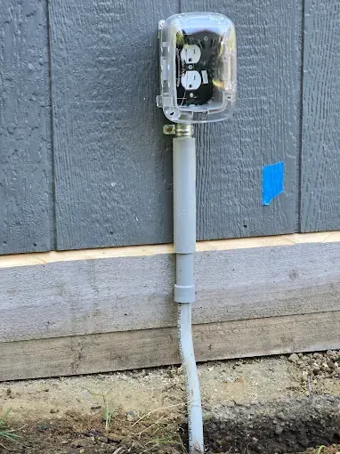 Outdoor electrical outlet with protective cover attached to a gray conduit on a building's exterior.
