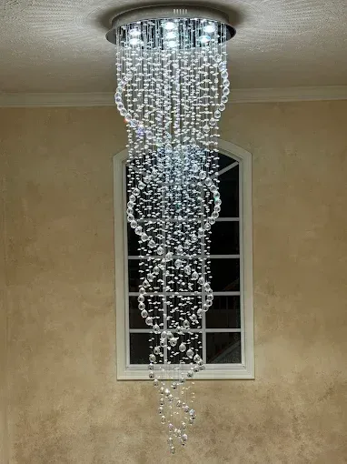 Crystal chandelier hanging in front of a window on a beige wall.