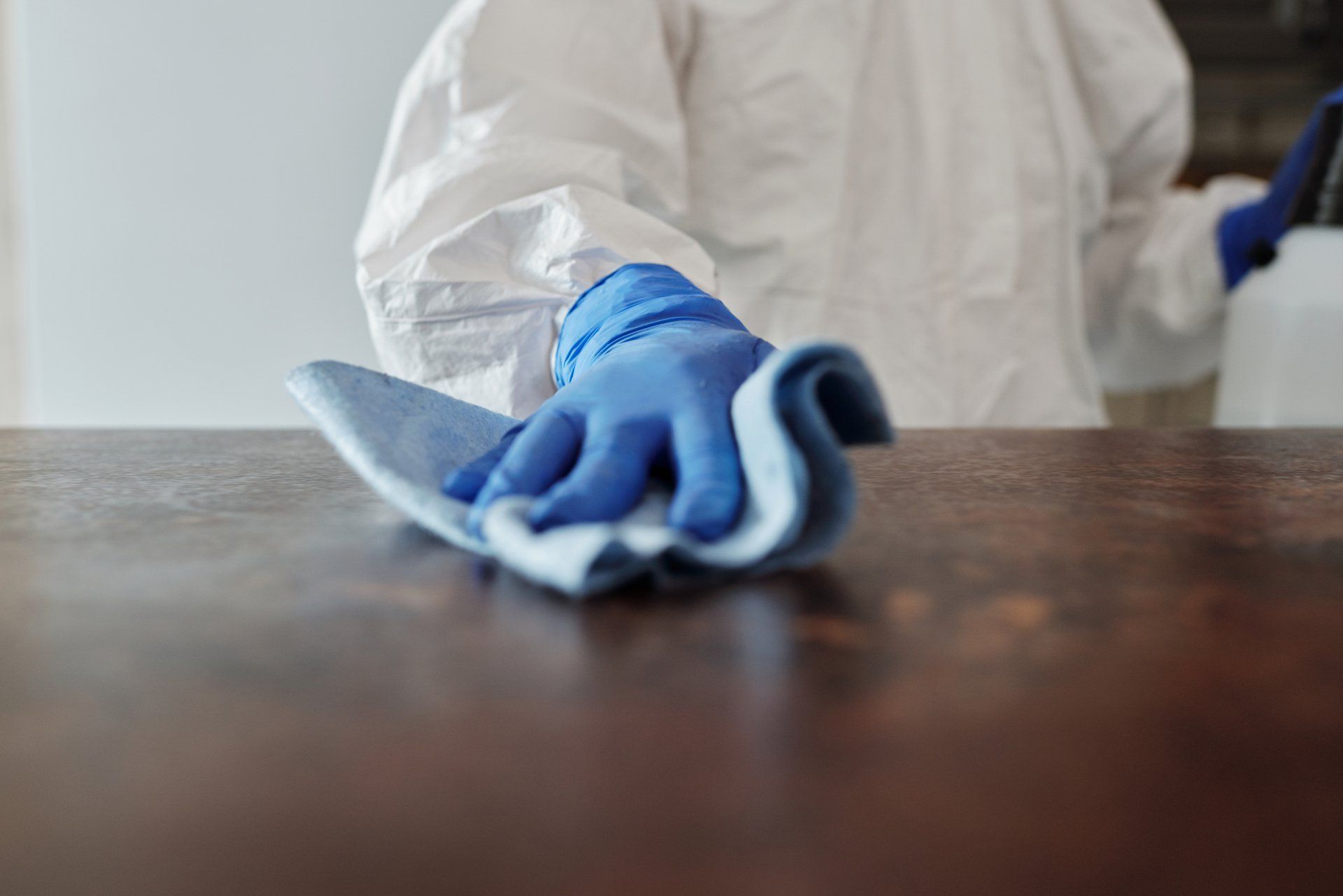 A person wearing blue gloves is cleaning a table with a cloth.