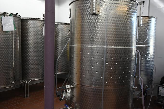 Several large stainless steel tanks with textured exteriors lined up in a winery storage room.