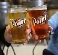 Two hands hold up glasses of light and amber beer, both featuring the Point Brewery logo, in a casual setting.