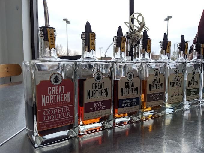 A row of Great Northern distillery bottles with pour spouts, arranged on a metal bar counter.