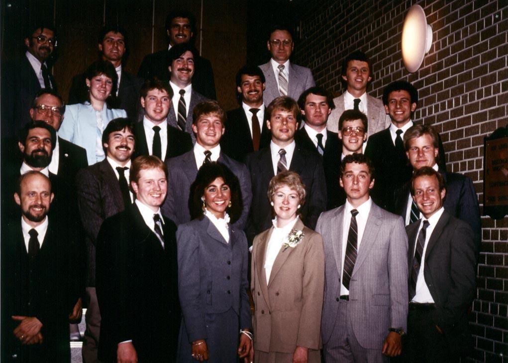 A group of twenty-four people in business attire posing for a formal portrait against a brick wall.