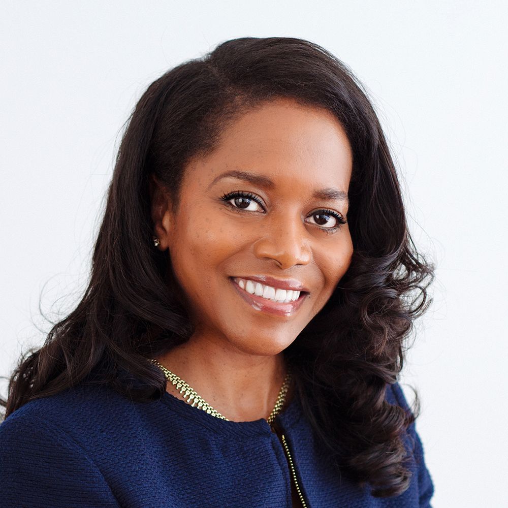Woman with dark hair smiles, wearing a navy blazer and gold necklace.