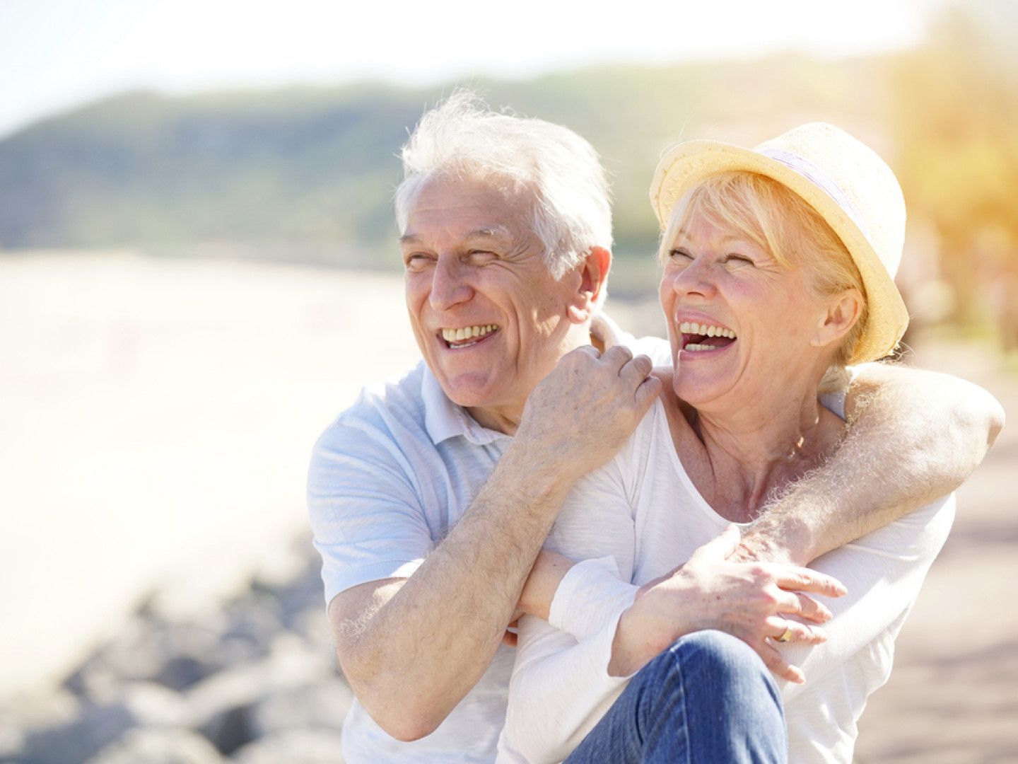 Smiling couple, man with arm around woman, by water, sunlight.