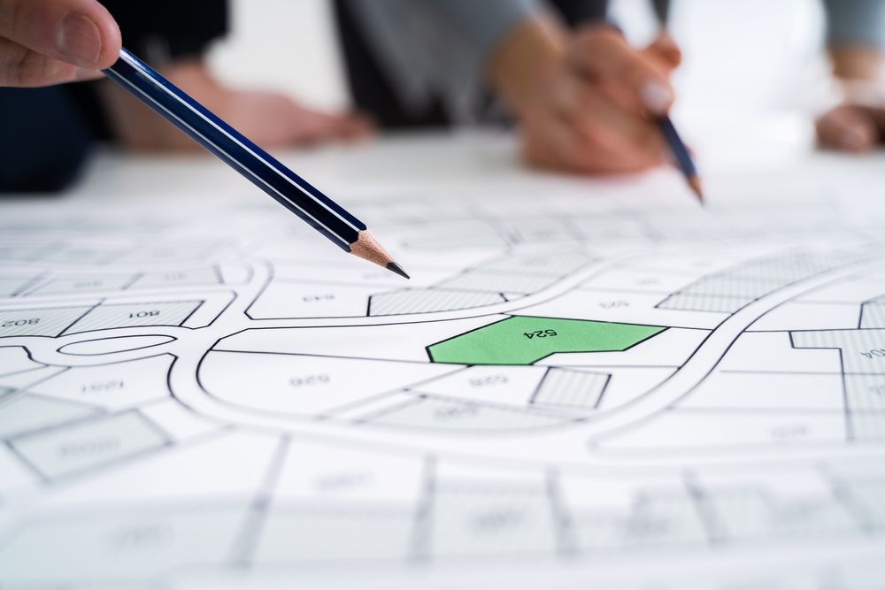 Two People Examining a Land Map, Pointing Pencils at a Highlighted Green Lot — Adamson Town Planning in Noosaville, QLD
