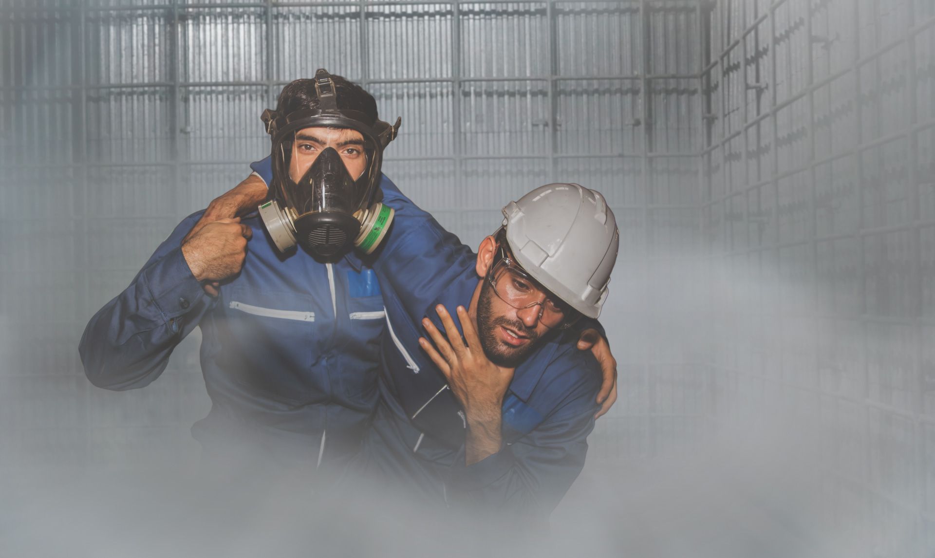 A man wearing a gas mask is carrying another man in a smokey room.