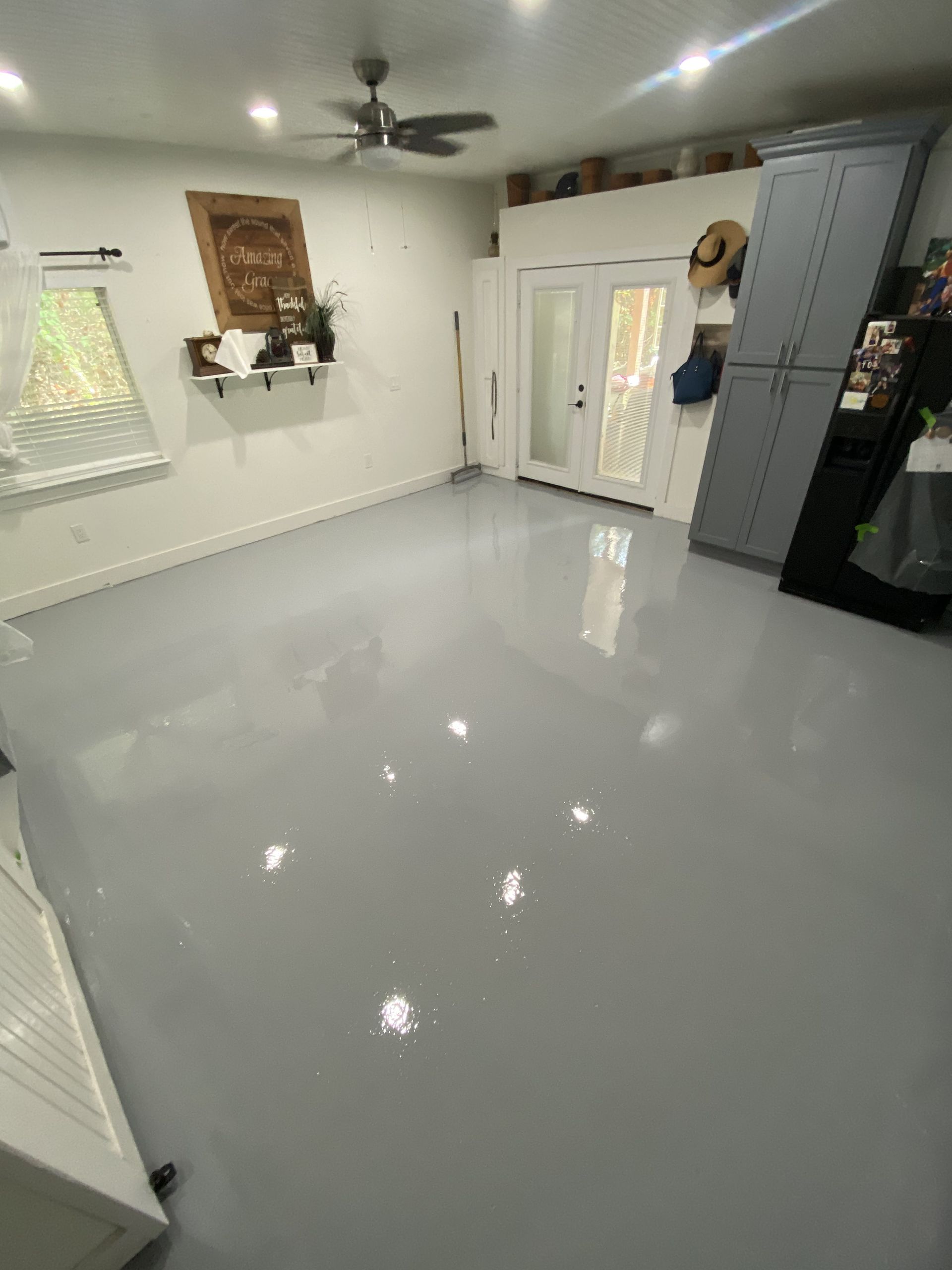A room with a gray epoxy floor. There is a ceiling fan, a cabinet, and a door visible.
