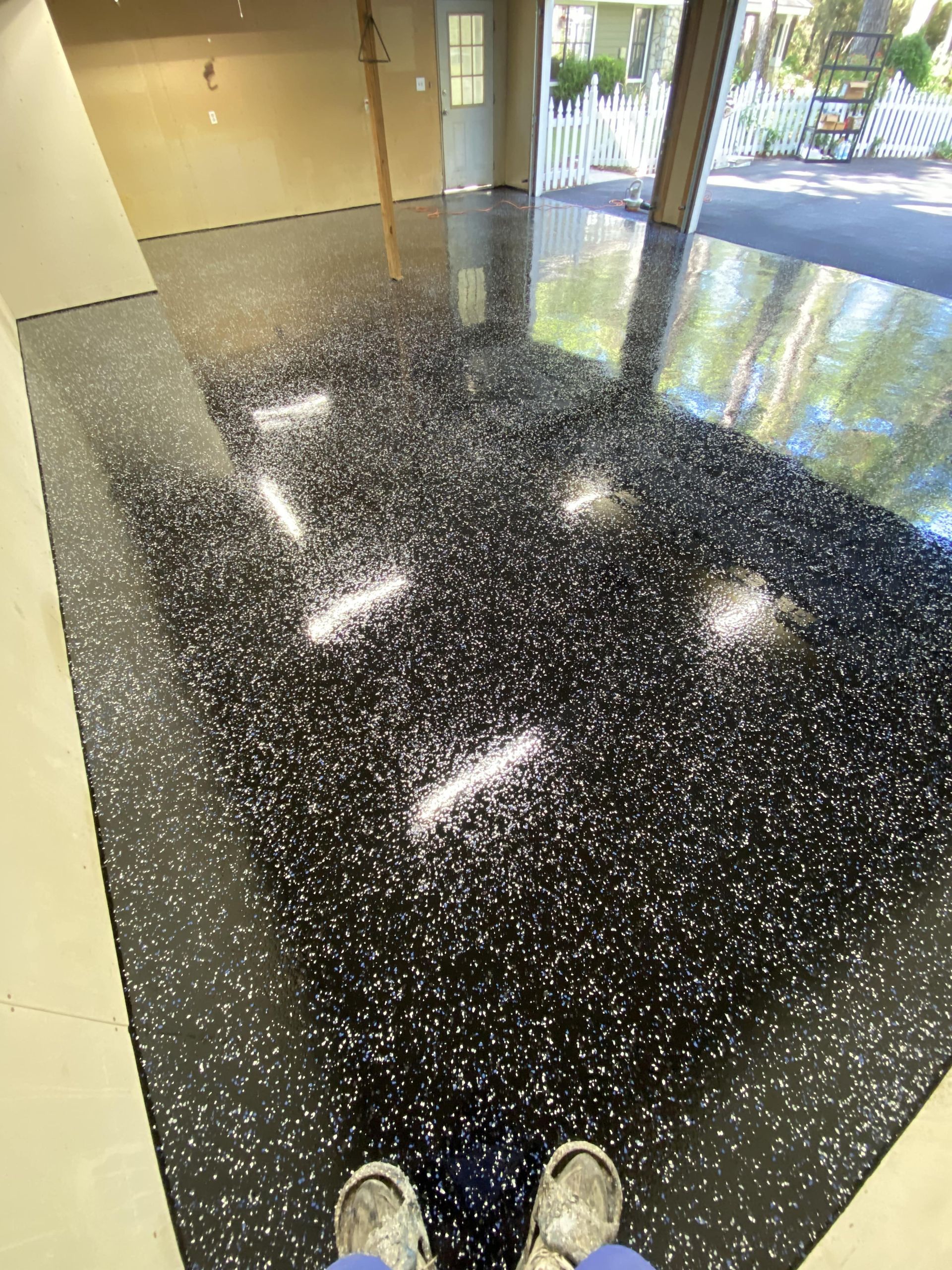 Person standing on a black epoxy floor with white flecks in a garage.