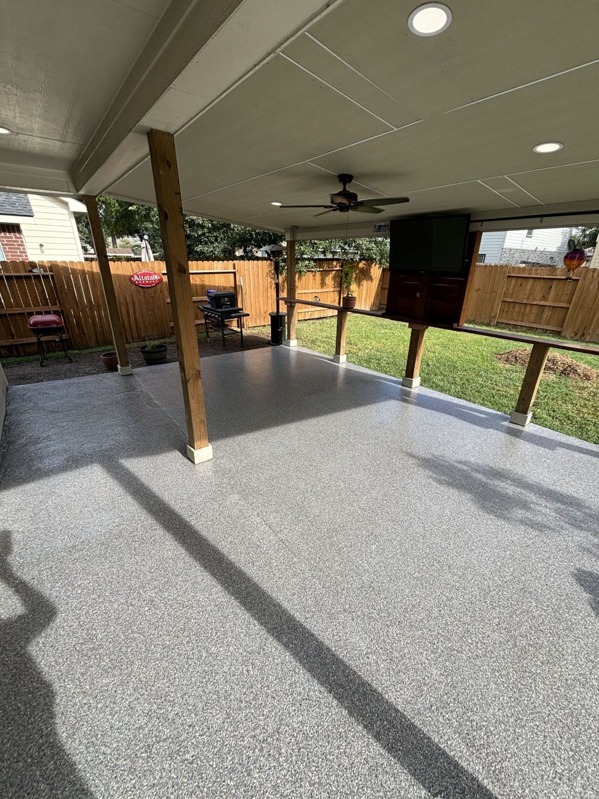 Covered patio with speckled gray flooring, wooden supports, and a mounted TV.