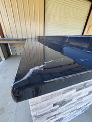 Black countertop with shiny finish, on stone-like base, against a corrugated wall.
