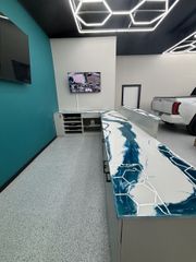 Room with a blue and white countertop, TV, and a white pickup truck in the background. Teal wall and speckled floor.