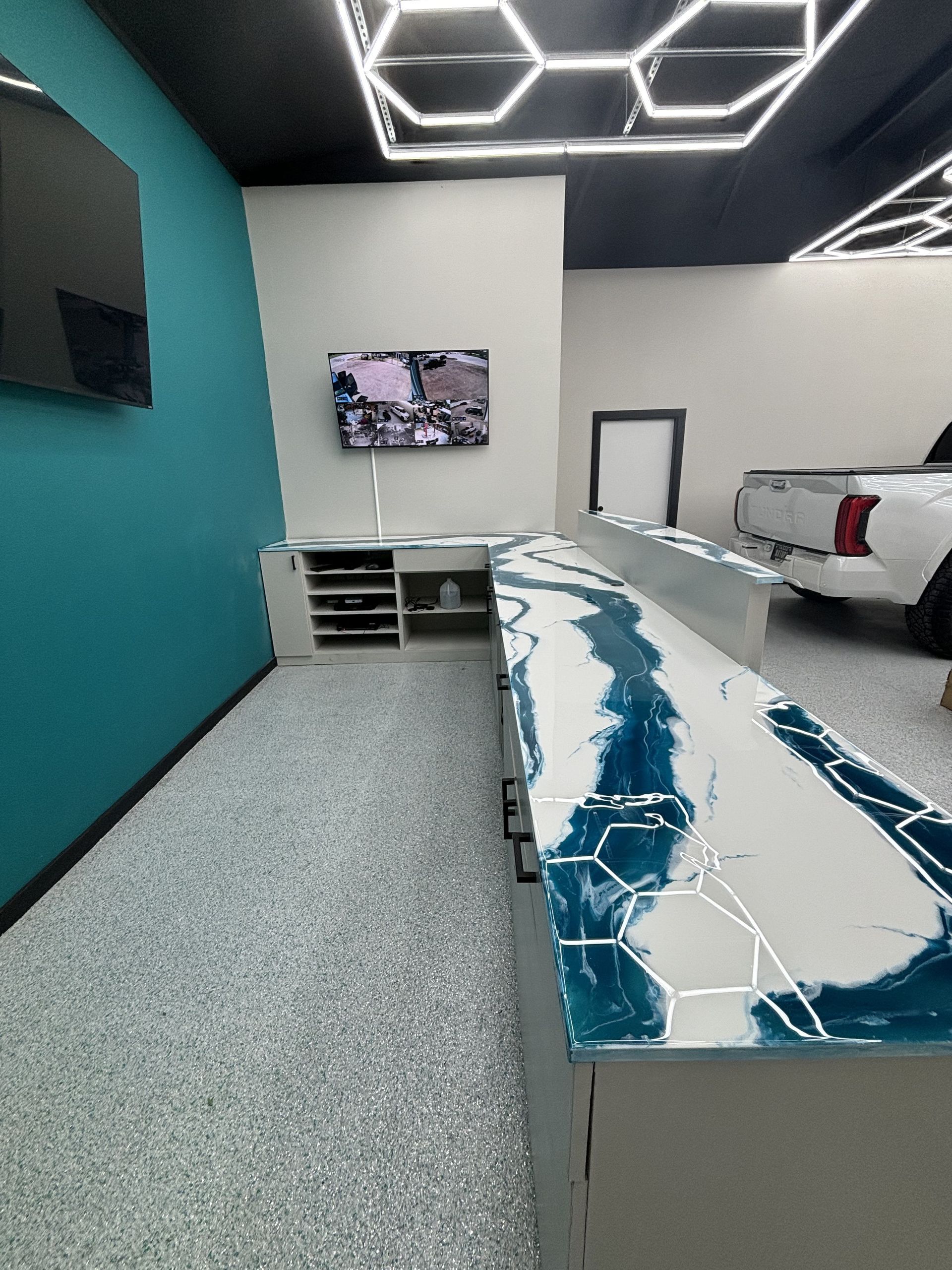 Room with a blue and white countertop, TV, and a white pickup truck in the background. Teal wall and speckled floor.