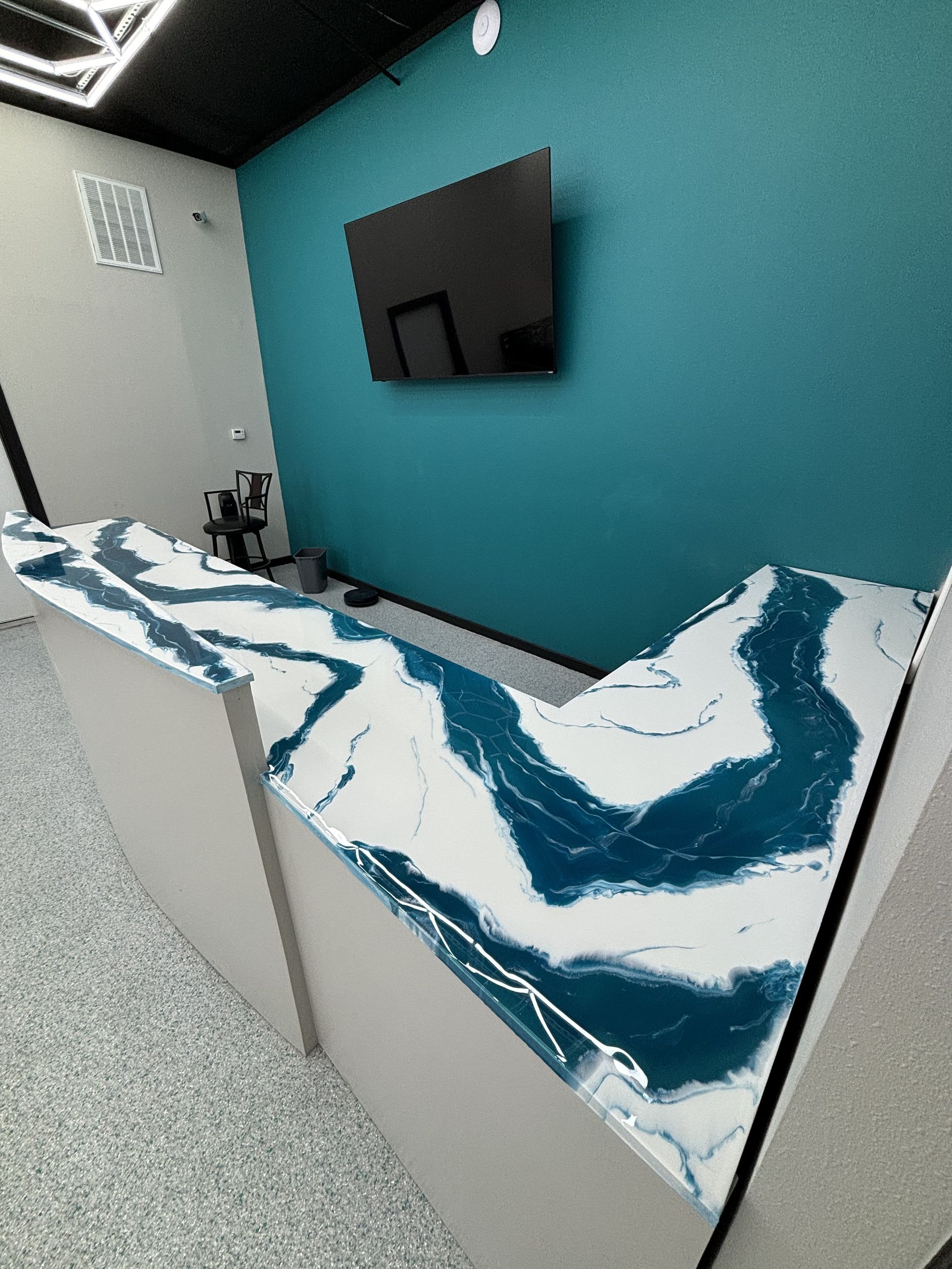 Reception desk with a blue and white swirled epoxy countertop, blue wall, and TV.