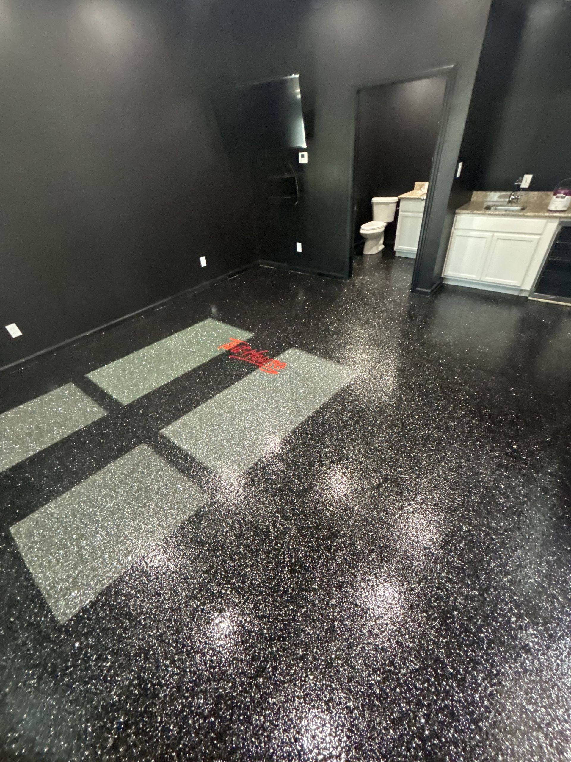Black room with glitter-covered floor, bathroom visible in the background, and sunlight shining in.